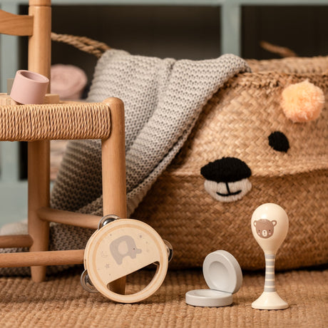 Bambino Wooden 3pc Music Set displayed on neutral beige carpet featuring a wooden rattle with elephant design, white suction cup bowl, and bear-themed rattle spoon, styled with natural wood furniture and plush brown teddy bear in background