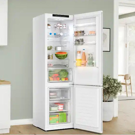 White Bosch Series 4 70/30 fridge freezer with both doors open displaying fresh produce, beverages and groceries in a modern kitchen with sage green walls and wooden flooring