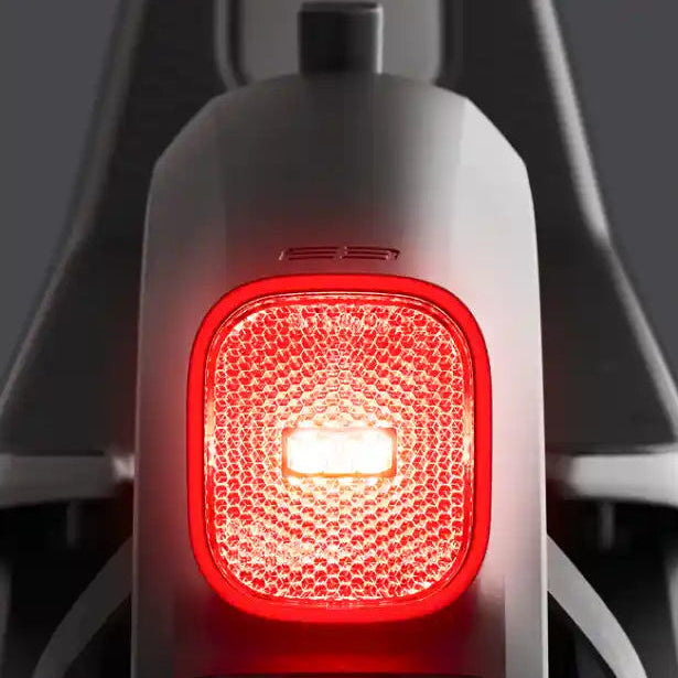 Close-up of red LED tail light on Segway Ninebot Kickscooter E3 Pro electric scooter showing illuminated safety light with white center against dark gray frame and black fenders
