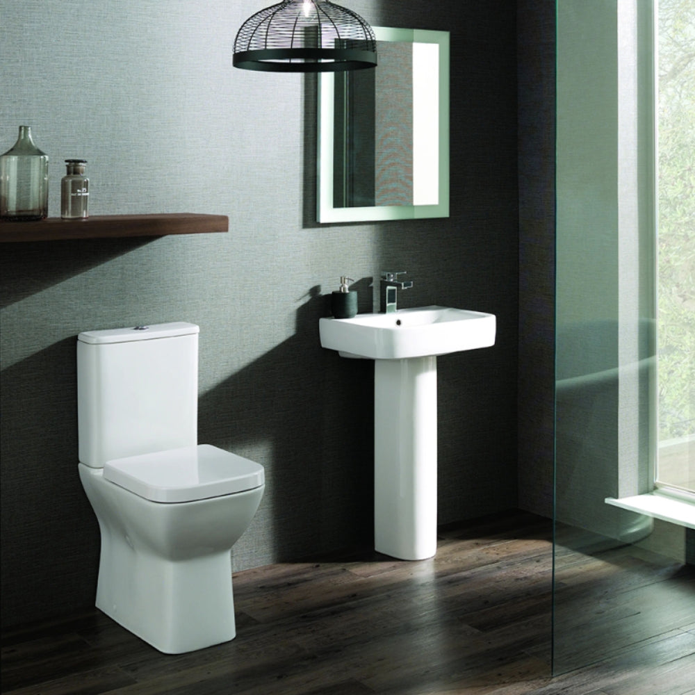Modern bathroom suite featuring a white comfort height toilet with soft close seat, matching white pedestal sink, and black wall-mounted mirror with LED lighting, set against dark charcoal and light grey textured walls with dark wood flooring