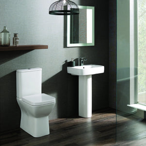 Modern bathroom suite featuring a white comfort height toilet with soft close seat, matching white pedestal sink, and black wall-mounted mirror with LED lighting, set against dark charcoal and light grey textured walls with dark wood flooring