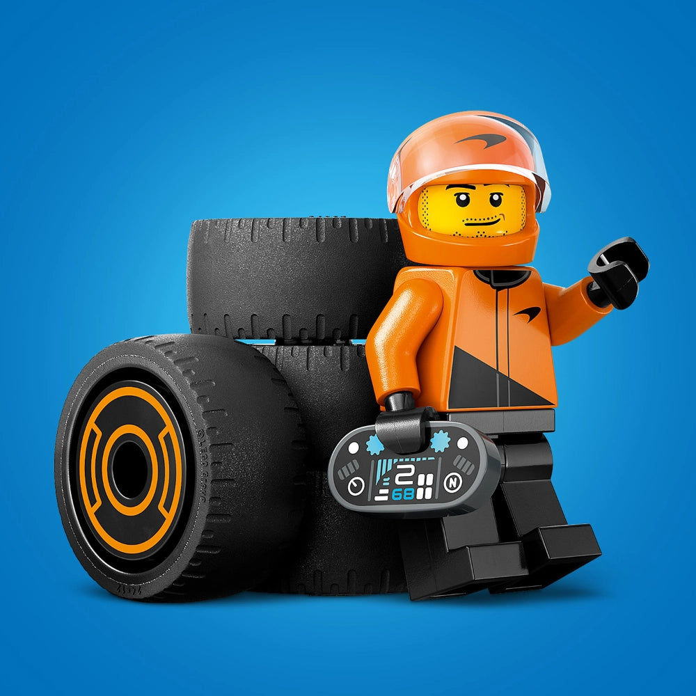 LEGO minifigure racing driver in bright orange helmet and suit with black gloves, standing next to large black racing tires with orange trim and a detailed gray digital dashboard, against a blue background