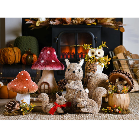 Handmade natural fiber hedgehog ornament with red ribbon displayed among autumn woodland decorations including mushrooms, owls, pinecones and wooden baskets on beige carpet with fireplace backdrop