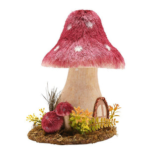 Handmade natural mushroom ornament with red and white spotted cap, wooden stem, surrounded by miniature moss, ferns and yellow flowers on a soil base