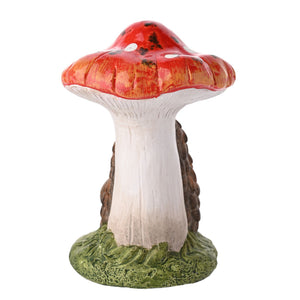 Decorative garden ornament featuring a red and white spotted toadstool mushroom with a hedgehog holding a pinecone against the stem, set on a green moss base, painted ceramic figurine