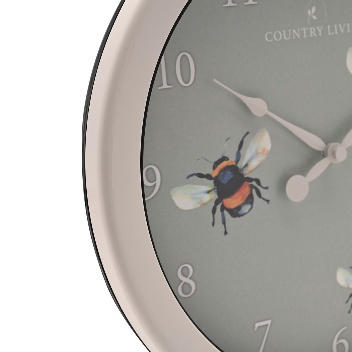 Close-up view of a Country Living outdoor clock with a grey dial featuring a colorful bee illustration, white numbers 6-10 visible, white metal hands, cream-colored rim, and black bezel, 26.5cm diameter
