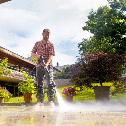 Man using a pressure washer on a patio with a garden and house in the background