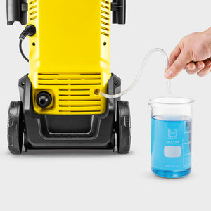 Yellow and black Karcher K3 pressure washer with blue cleaning solution in measuring beaker, demonstrating water and detergent mixing for the eco-friendly power washer