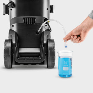 Karcher K7 WCM Flex Eco Booster power pressure washer shown from front view with black and silver cylindrical body, wheeled base, and blue cleaning solution being added via dropper into measuring beaker