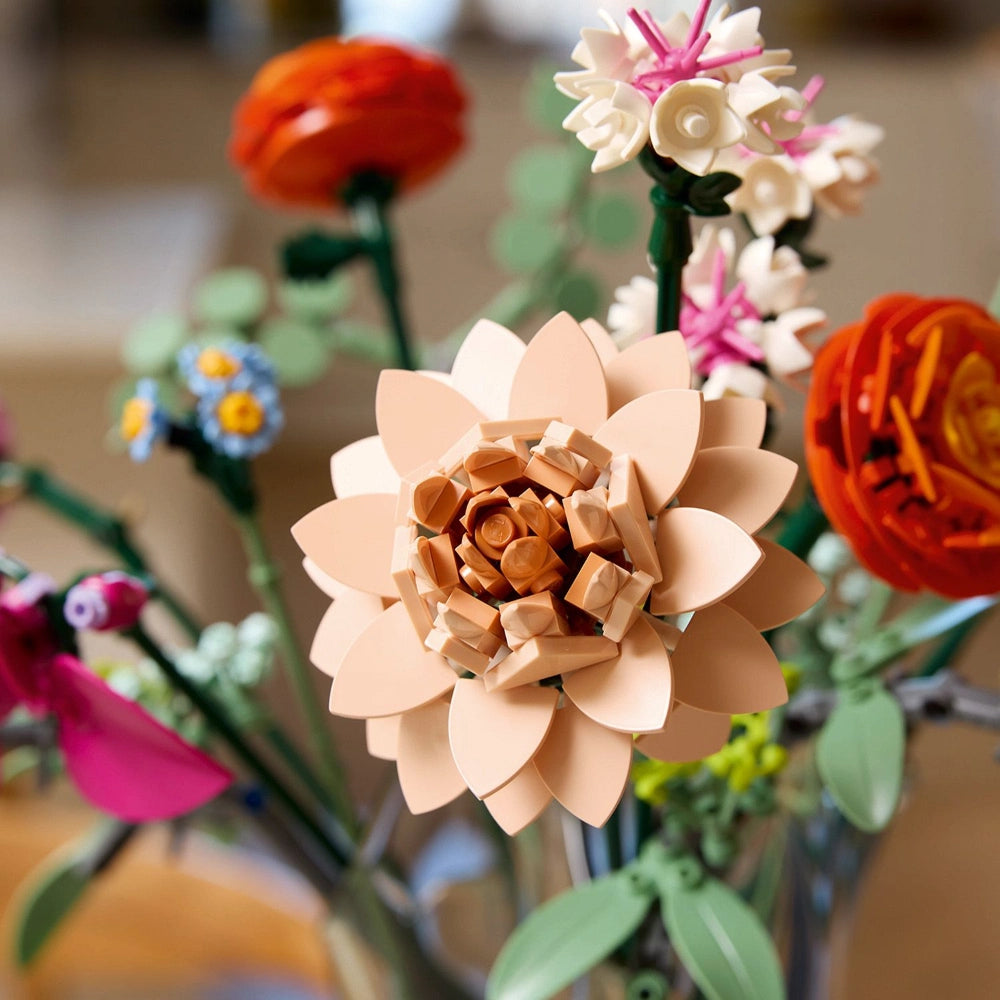 LEGO paper craft flower bouquet featuring a peach-colored dahlia in focus with layered petals, surrounded by colorful artificial flowers including red roses, pink blooms, white daisies, and green stems arranged in a decorative display