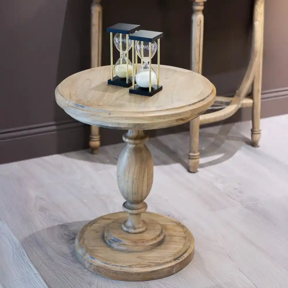 Natural wood round pedestal side table with turned column base displaying two black-framed hourglass timers on top, featuring traditional farmhouse style design in light oak finish