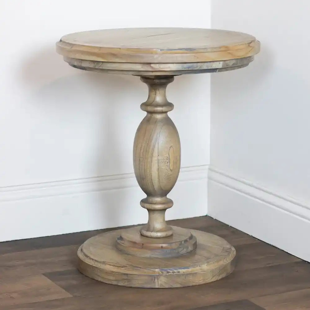 Tara Lane round pillar side table in natural wood with oval pedestal base and circular top, displayed in white interior corner