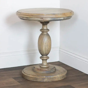 Tara Lane round pillar side table in natural wood with oval pedestal base and circular top, displayed in white interior corner