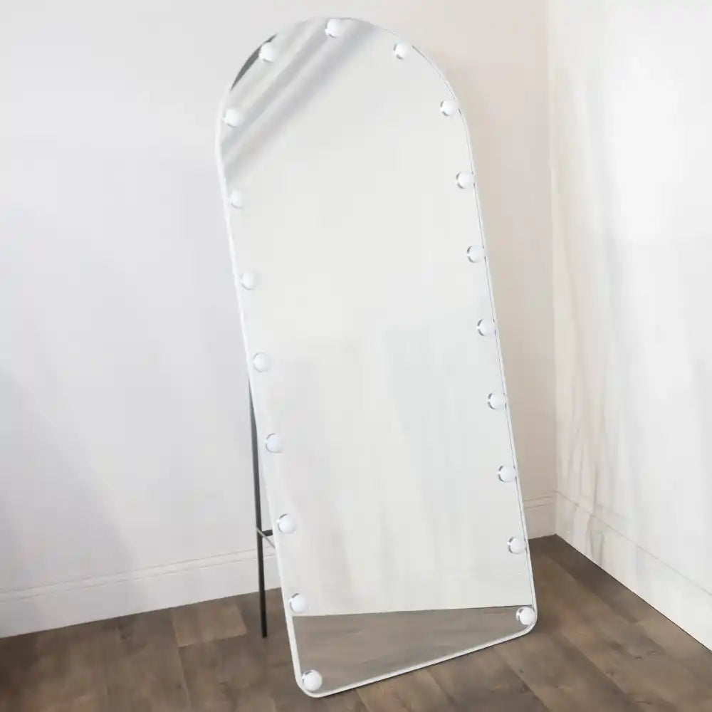 White arched freestanding mirror with LED bulbs around frame, 170cm tall, leaning against white wall on wooden floor
