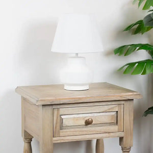 Tara Lane Marwood light wood 1 drawer end table with turned legs topped with white table lamp and green potted plant against white wall