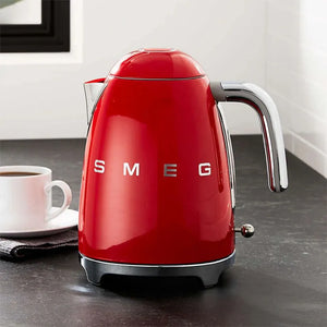 Red Smeg 1.7 litre retro 50s style kettle with chrome handle and base displayed on dark countertop next to white cup and saucer
