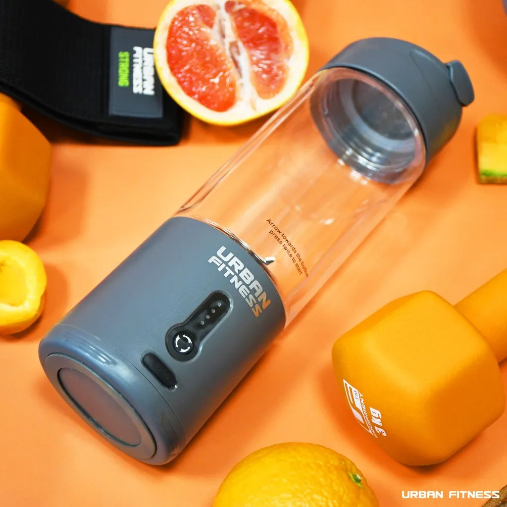 Urban Fitness VitalFuse portable blender in grey with control button displayed on orange background surrounded by fresh citrus fruits including grapefruit halves and lemons