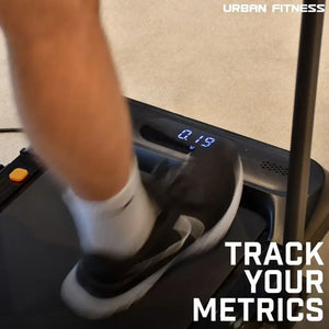 Person wearing white socks and light-colored pants on Urban Fitness walking treadmill with digital display showing 2.19 speed, black frame with orange button, beige wall background, track your metrics text overlay