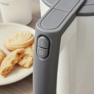 Morphy Richards Compact Travel Jug Kettle in white and grey with power button visible, displayed next to a plate of biscuits and a white mug