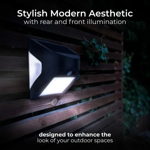Luceco Prysm black solar LED wall light with PIR sensor mounted on wooden fence boards at night, showing bright white front illumination and ambient rear glow, surrounded by climbing ivy