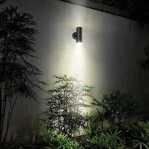 Luceco Azurar black stainless steel up down external wall light mounted on white wall illuminating green foliage and plants below