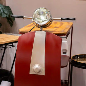 Red and white Vespa scooter-shaped wine rack with chrome headlight, handlebar grips, and white central stripe, displayed on wooden table in modern interior setting