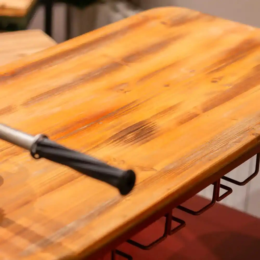 Wooden table surface with brush applying stain or finish and metal wine rack holder in red visible below