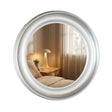 Round champagne-framed mirror reflecting a bedroom with wooden nightstand, table lamp, potted plant and curtains, 90cm Tara Lane Lyla design