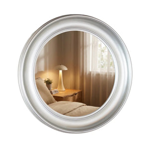 Round champagne-framed mirror reflecting a bedroom with wooden nightstand, table lamp, potted plant and curtains, 90cm Tara Lane Lyla design