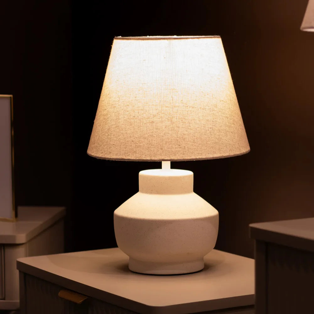 White ceramic bedside lamp with cream linen ombre shade, 36cm height, modern rounded base design on wooden table against dark background