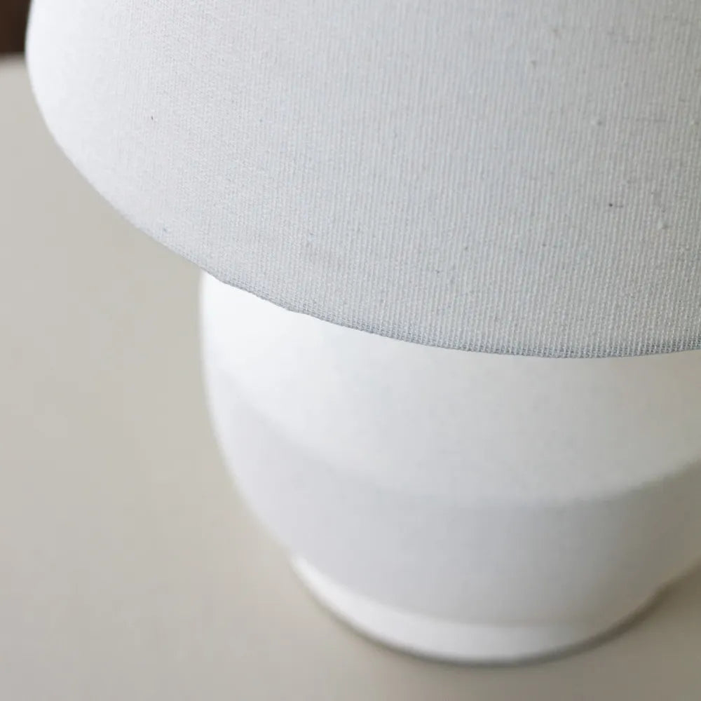 White ceramic bedside lamp with fabric shade showing close-up detail of textured linen material and smooth ceramic base