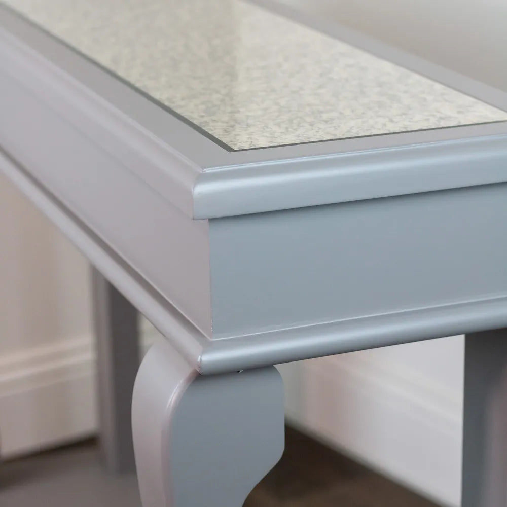 Close-up detail of Tara Lane Scroll Console Table showing antique mirror top surface, mink-colored wooden frame with decorative curved leg, and silver-toned metal edging and trim