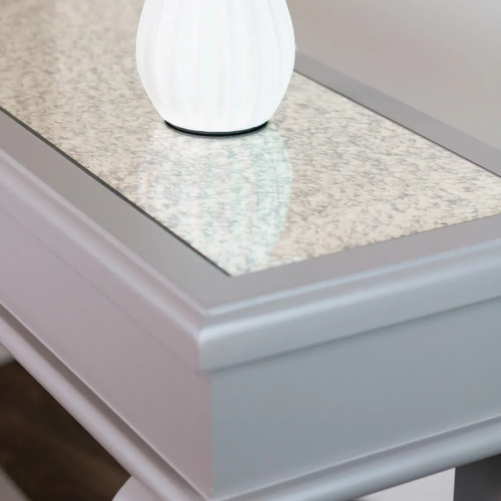 White globe table lamp on mink-colored console table with light gray speckled stone top and antique mirror inset