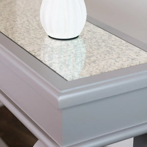 White globe table lamp on mink-colored console table with light gray speckled stone top and antique mirror inset