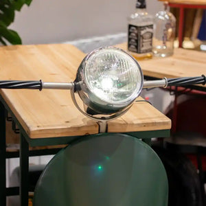 Green Vespa scooter-style wine rack with chrome headlight and wooden seat table top, displayed in a bar setting with bottles and bar accessories