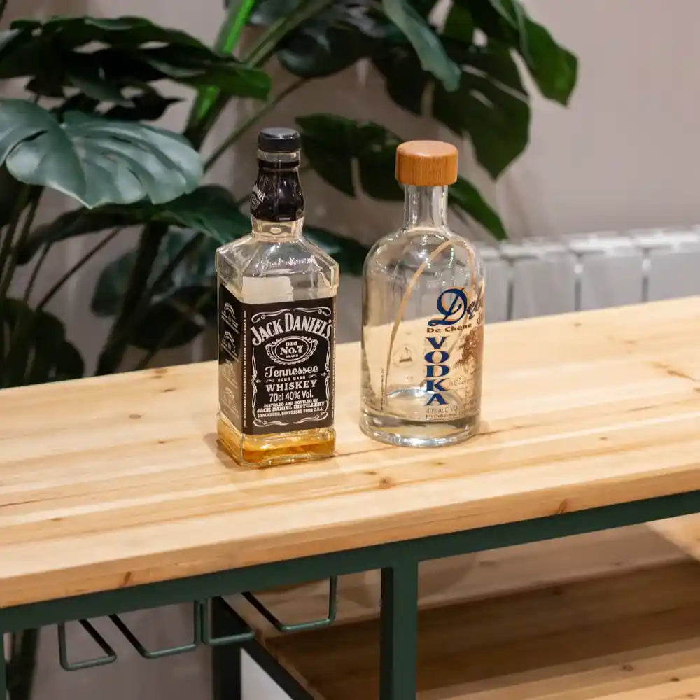 Wooden bar table with green metal frame displaying Jack Daniel's and Dooyk vodka bottles beside potted green plants
