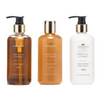 Three-piece Newgrange Living White Tea and Neroli body care set in 285ml bottles including hand wash in amber glass with pump dispenser, body wash in tan glass with pump dispenser, and moisturising body lotion in white glass with pump dispenser, all featuring gold-tone caps and black pumps
