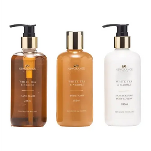 Three-piece Newgrange Living White Tea and Neroli body care set in 285ml bottles including hand wash in amber glass with pump dispenser, body wash in tan glass with pump dispenser, and moisturising body lotion in white glass with pump dispenser, all featuring gold-tone caps and black pumps