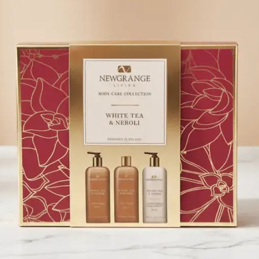 Newgrange Living White Tea and Neroli body care collection gift set featuring three 250ml bottles in gold and cream packaging with burgundy floral patterned box displayed on marble surface