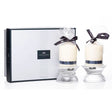 Newgrange Living Emma Pillar Candle Pair in cream white with dark navy ribbon bows, presented in clear glass holders with pleated design, accompanied by luxury black and white branded gift box packaging