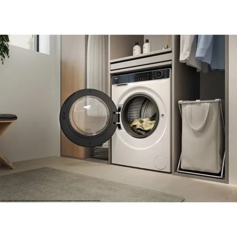 Haier X Series 9kg white front-load washing machine with black trim and open door displaying drum, positioned in modern laundry room next to dryer and laundry basket