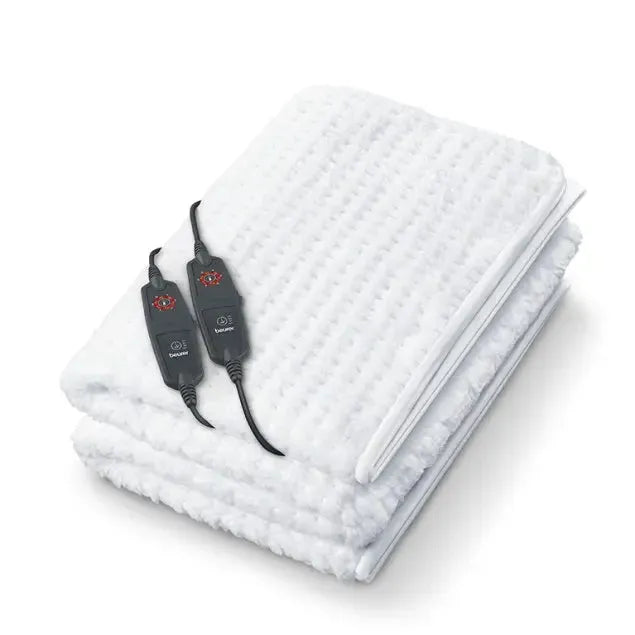 White quilted electric under blanket with dual control black remote controls featuring temperature settings displayed on top of folded blanket layers