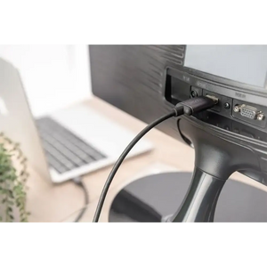 Black USB-C to HDMI adapter cable connected to a monitor with VGA port in an office workspace with laptop and potted plant visible in background
