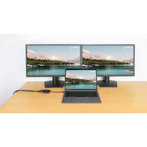 Manhattan USB C to Dual HDMI adapter connecting a gray laptop to two black monitors on a wooden desk, displaying a scenic mountain and lake landscape wallpaper across all three screens