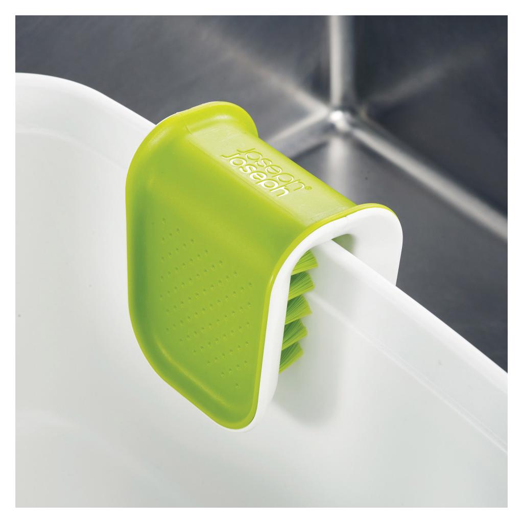Joseph Joseph BladeBrush green and white knife cleaner with integrated brush bristles mounted on white sink rim against dark background