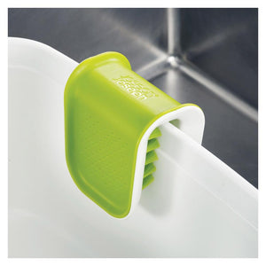 Joseph Joseph BladeBrush green and white knife cleaner with integrated brush bristles mounted on white sink rim against dark background