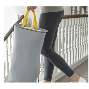 Person carrying grey Joseph Joseph Tota 60 litre laundry basket with yellow handles down white staircase with wooden banister
