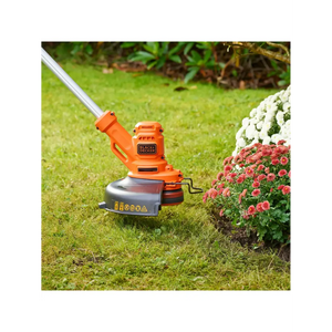 Black & Decker BESTA525 orange and grey electric grass strimmer with cutting head positioned on lawn next to pink and white flowering plants in garden setting
