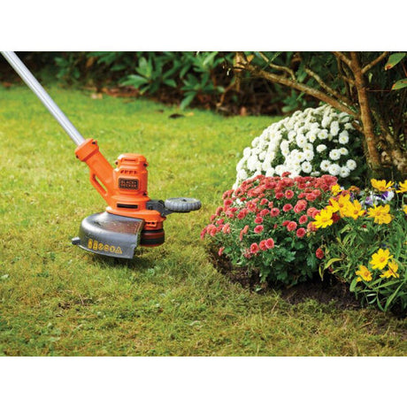 Black and Decker BESTA530 orange corded grass strimmer in use on lawn next to flower bed with white, red and yellow flowers