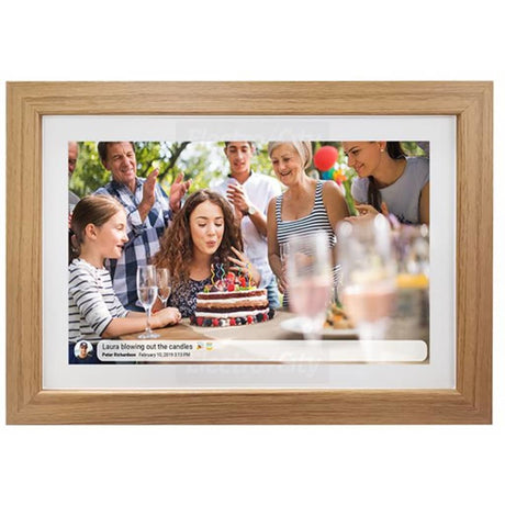 Light oak wooden digital photo frame displaying a birthday party scene with a girl blowing out candles on a decorated cake surrounded by family and friends, with white mat border and social media post caption visible at bottom